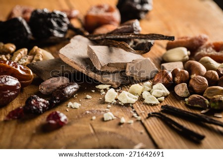 Raw cocoa mass and cocoa butter with hazelnuts, walnuts, cashews and vanilla orchid pod on the grunge table or desk in the kitchen. Composition of the ingredients for cooking cakes or ice cream.