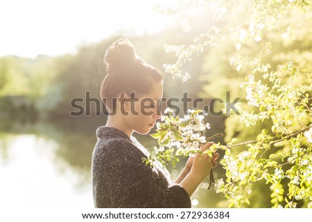 Beautiful black hair woman enjoying blooming tree from profile, pretty girl relaxing outdoor.  Happy young lady and spring green nature. Low depth of field. Strong back light.