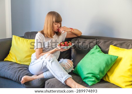 Young girl sitting on the couch and eating strawberries