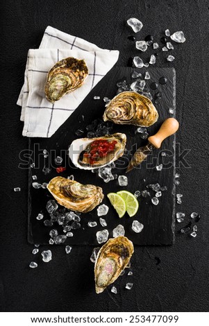Fresh oysters with tomato salsa on a black stone plate top view