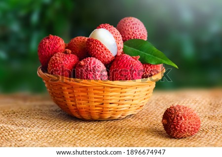 Front view of fresh ripe lychee fruit and peeled lychee with green leaves on wooden bowl and blur garden background. 