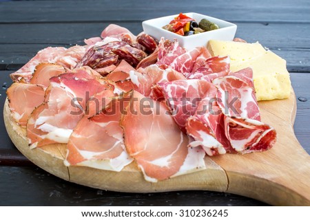 typical Italian appetizer with salami, cheese and pickles in a wooden cutting board