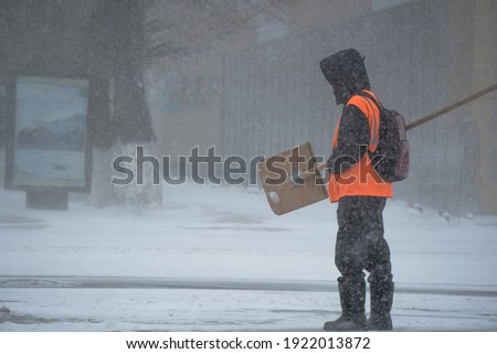 A working man of the municipal service with a snow shovel walks along the road in a storm, blizzard or snowfall in winter in bad weather in the city.Extreme winter weather conditions in the north. Foto stock © 