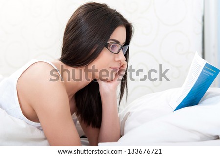 Image of a woman who reads a book in bed with glasses