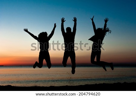 Silhouette of friends jumping on beach during sunset time