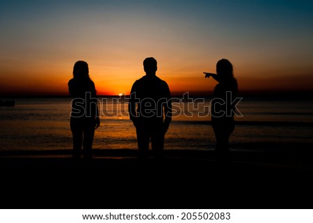 Silhouette of three friends in the morning at the beach waiting for the sunrise.