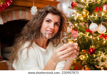 Portrait of smiling young woman decorating the Christmas tree over living room holding a small candel