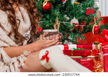 Close-up of young woman legs and hands, holding a mug of tea near  Christmas tree, over living room,focus on christmas tree!