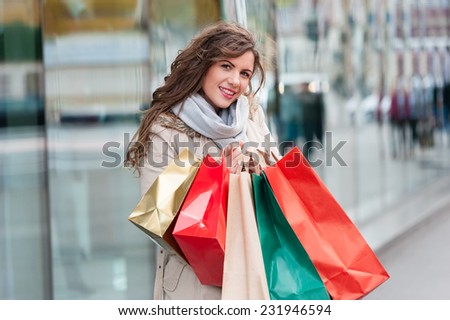 Photo of young joyful woman with shopping bags on the background of shop windows. Outdoors.