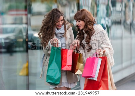 Two beautiful women looking inside shopping bags in the city over shop windows background