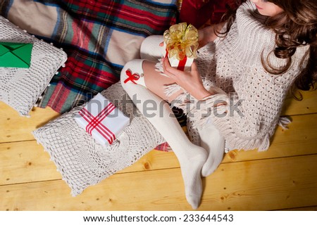 Close-up of young woman legs holding gift box, lying on carpet at the Christmas tree over living room.