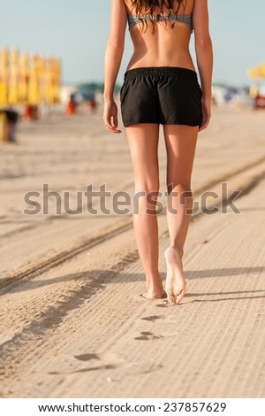 Woman walking on beach at sunrise during work out training. Fit beautiful young female model jogging