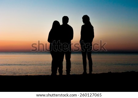 Silhouette of a couple and a friend in the morning at the beach looking at sunrise . Support, together, winning, helping, freedom concept.