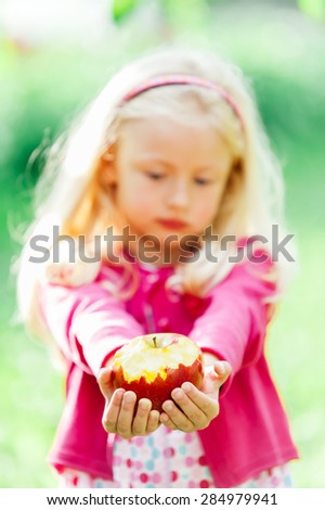 Pretty little blonde girl holding a bitten apple, an looking sad
