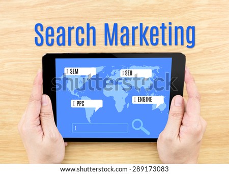Hand holding tablet with Search Marketing word on wooden table,digital business concept