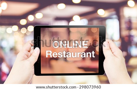 Hand hold tablet with Online restaurant word on screen with blur restaurant background.