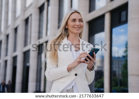 Purposeful young caucasian blonde woman in white suit standing outdoor with phone on summer shiny day. Happy student swedish girl going to call her boyfriend. Cute smiling Italian pretty woman. Foto stock © 