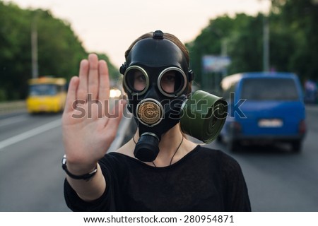 Ecological concept of air contamination. Woman in gas mask near highway showing stop gesture