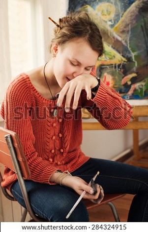 Portrait of beautiful woman artist with quirky expressions and touching her face and scratching her nose in home art studio