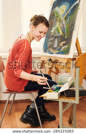 Smiling girl paints on canvas with oil colors in her workshop