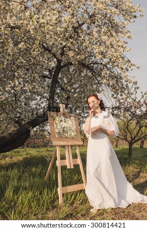 Beautiful woman artist drawing her picture on canvas with oil colors in the garden