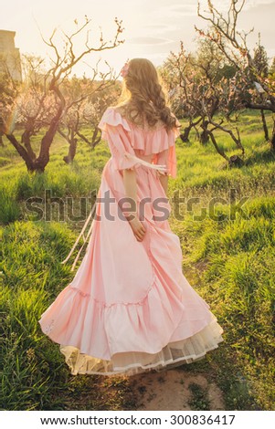 Attractive woman in pink dress enjoying the nature and walking in the bloom garden on sunset. Freedom concept