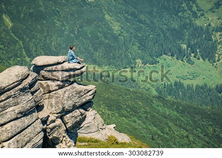 Man sitting on a rock in the lotus position and looking at the sky
