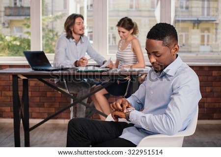 African american man sitting on the chair in business office and waiting for job interview looking at the clock
