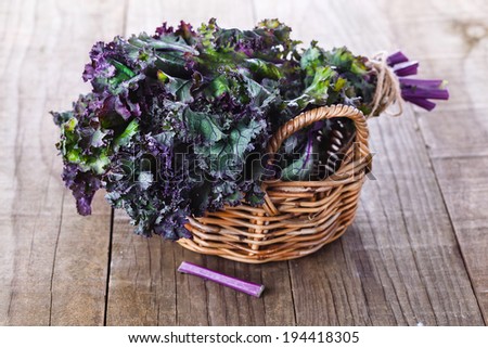 Bunch of organic kale in a woven basket on a rustic wooden background. Selective focus, shallow dof