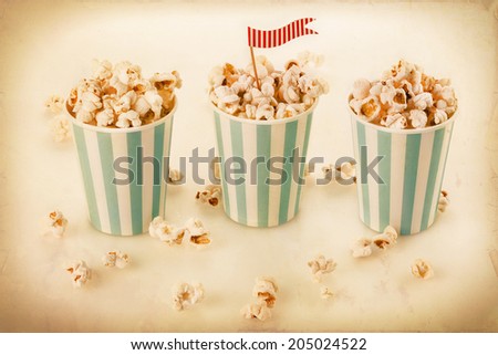 Retro style image of Buttered popcorn in vintage striped blue-white cups with decorative flag. Selective focus, vintage filters, textures