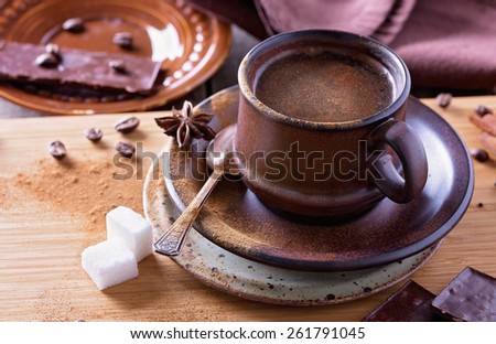 Spiced coffee in a textured ceramic cup with cinnamon powder, anise stars, sugar and pieces of chocolate over wooden table closeup. Selective focus, shallow depth of field
