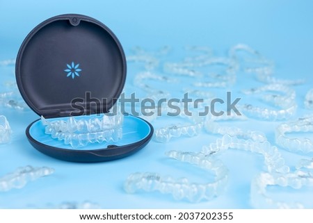 Invisible retainers case with orthodontic aligner brackets thrown around. Black plastic dental container for invisalign braces on blue background Stock foto © 