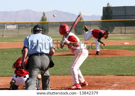 baseball in mid-air pitched to batter with back-side view of batter, catcher and umpire at Cochise College baseball game