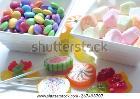 Two ceramic bowls of colored smarties, sour candies, lollipop and gummy bears on white background