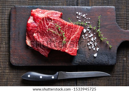 Beef cut: raw flat iron steaks of corn-fed cows on a dark wooden cutting board on a dark wooden background with fresh rosemary, sea salt, olive oil, peppercorns, garlic, view from above ストックフォト © 