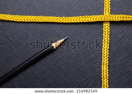 Gold color rope cable and pencil close up photo put on the black color artificial leather surface background.