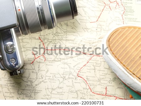 Green color sport shoe with orange color shoe cable and camera put on old  and vintage paper map represent the detail of city name and destination.