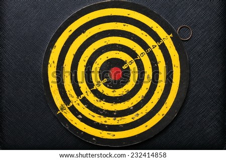 Used and vintage dartboard with a lot of damaged hole from arrow marked put on the black color leather surface as a background represent the entertainment game.