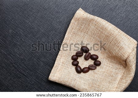 Coffee bean arrange to the shape of heart put on the coffee bean sack in the scene appear the back color leather background.