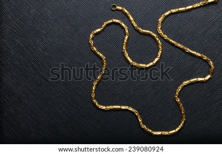 Gold necklace arrange to the line and curve shape pattern put on black color leather background represent the abstract meaning.