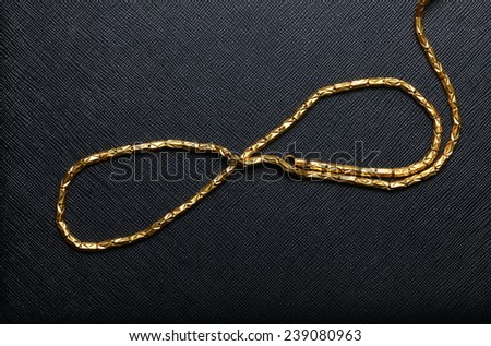 Gold necklace arrange to the line and curve shape pattern put on black color leather background represent the abstract meaning.
