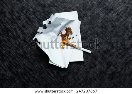 Gold color stain on the trash paper with plastic stirring rod put on the black color leather surface background represent the model making material.