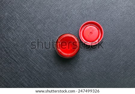 A bottle of red color for plastic model paint with bottle lid put on the black color leather surface background represent the model making material.