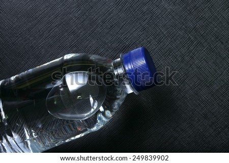 Drinking water bottle with blue color cap made from transparent food grade plastic put on the black color leather background represent the water containing material related.