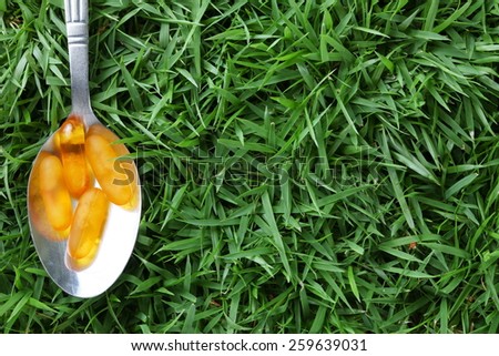 Vitamin yellow color capsule in the table spoon put on grass background represent the medicine and vitamin related.