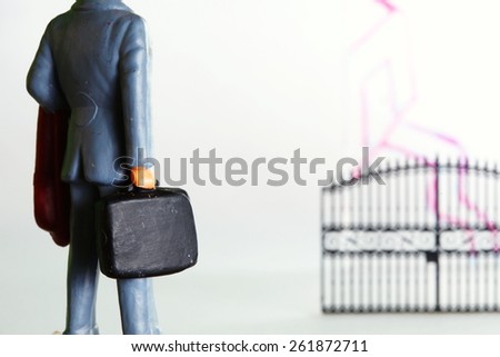 The figure businessman plastic model and plastic gate model in the scene appear the hand drawing house shape on clear acrylic surface represent the mortgage concept idea.