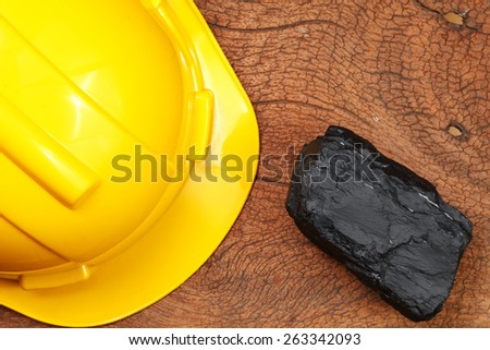 British coal element beside safety helmet  put on the hard wood brown color surface as a background represent the construction material. Super macro shot and intention focus at the coal.