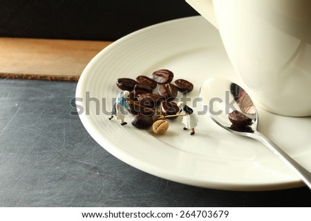 Coffee beans put on the ceramic saucer with spoon in the scene appear farmer miniature figure model also represent coffee concept related idea .Super macro shot and intention focus at the coffee bean.