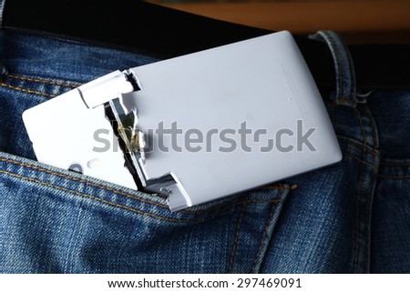 Blue denim jeans in dark color in the scene present the old denim look at the back pocket part with broken mobile phone inside.