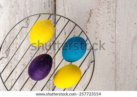 Colored easter eggs on metallic rack on wooden white shabby background
